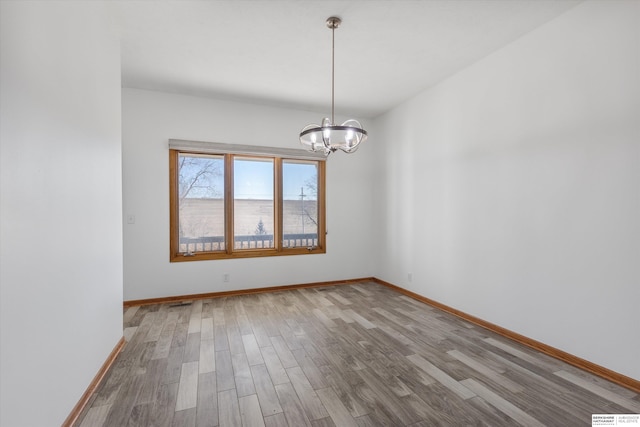 spare room with wood-type flooring and an inviting chandelier