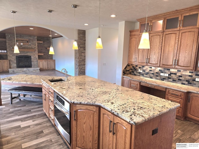 kitchen featuring a kitchen island with sink, oven, sink, hanging light fixtures, and a fireplace