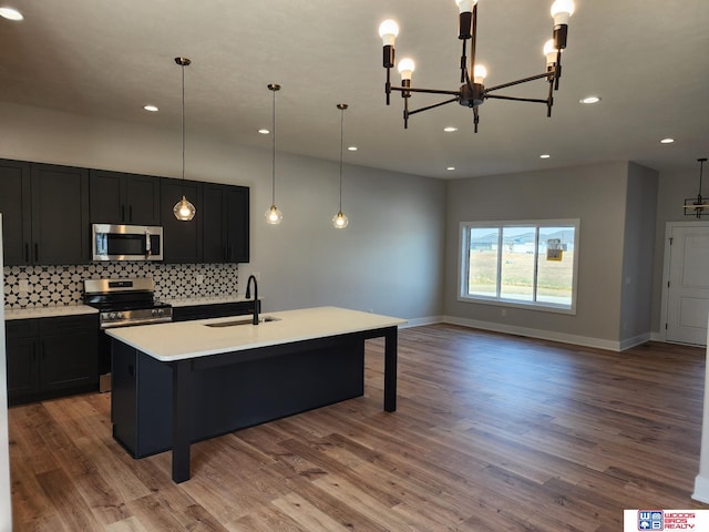 kitchen with light wood-type flooring, stainless steel appliances, a kitchen island with sink, sink, and pendant lighting