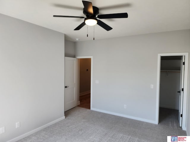 unfurnished bedroom with a closet, a walk in closet, light colored carpet, and ceiling fan