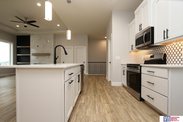 kitchen featuring decorative backsplash, appliances with stainless steel finishes, white cabinetry, hanging light fixtures, and an island with sink