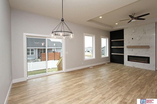 unfurnished living room with built in shelves, a high end fireplace, ceiling fan with notable chandelier, and light wood-type flooring