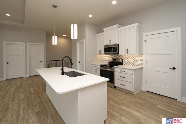 kitchen with stainless steel appliances, sink, decorative light fixtures, white cabinets, and an island with sink