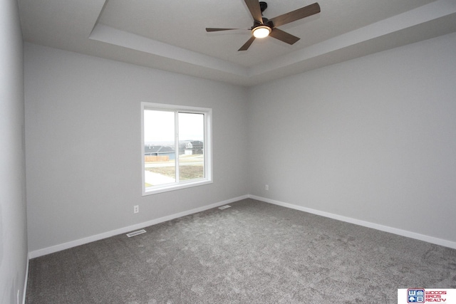 empty room featuring ceiling fan, dark carpet, and a tray ceiling