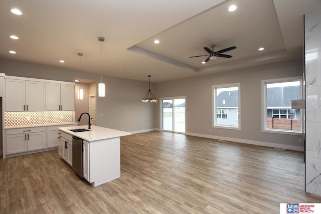 kitchen with ceiling fan with notable chandelier, a raised ceiling, sink, decorative light fixtures, and an island with sink