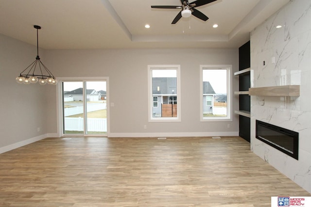 unfurnished living room with built in shelves, a raised ceiling, a premium fireplace, light hardwood / wood-style floors, and ceiling fan with notable chandelier