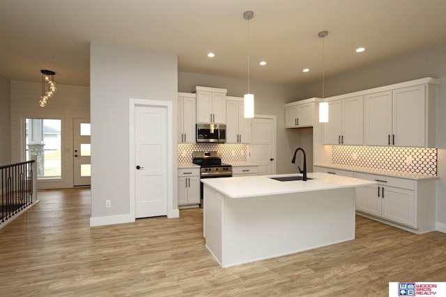 kitchen with pendant lighting, stainless steel appliances, sink, and an island with sink