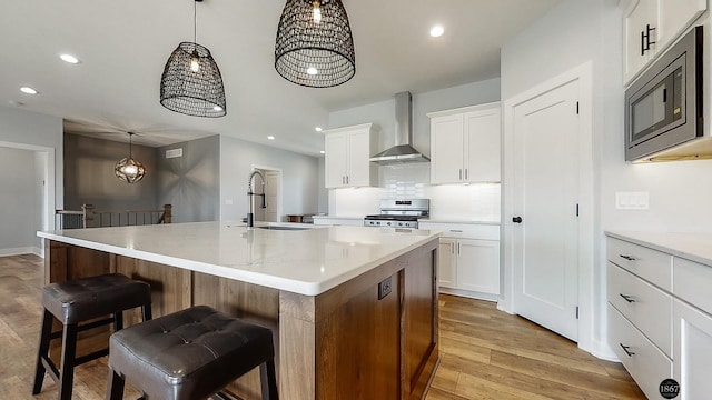 kitchen with wall chimney range hood, sink, stainless steel gas stove, built in microwave, and an island with sink