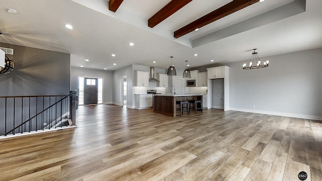 unfurnished living room with beamed ceiling, a chandelier, light hardwood / wood-style flooring, and sink