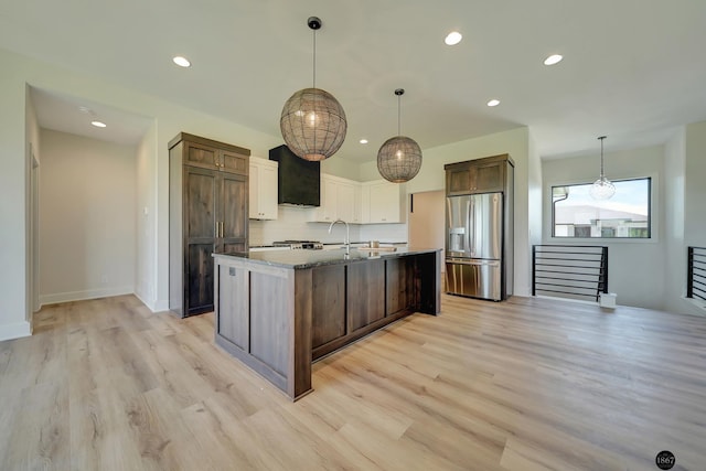 kitchen featuring pendant lighting, stainless steel refrigerator with ice dispenser, an island with sink, tasteful backsplash, and light hardwood / wood-style floors