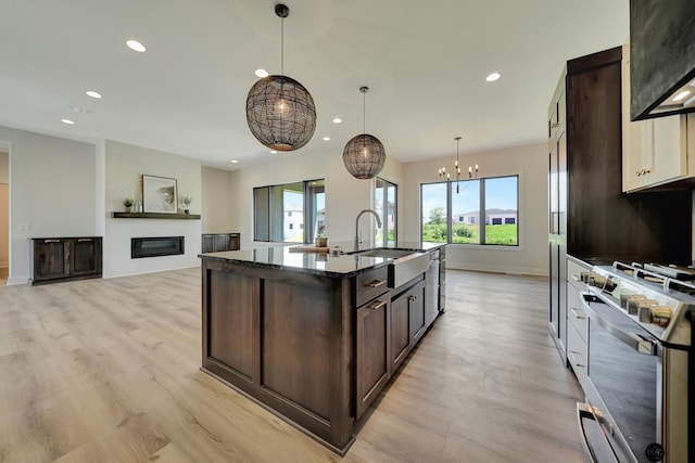 kitchen with high end range, dark brown cabinets, light hardwood / wood-style floors, and an island with sink