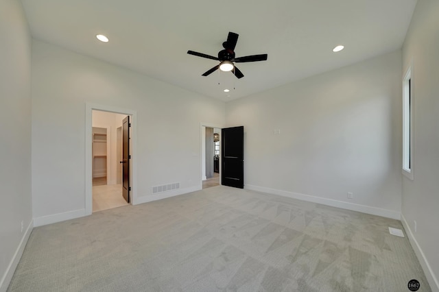 unfurnished bedroom with ceiling fan, a spacious closet, light carpet, and a closet