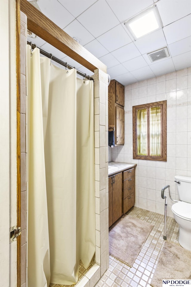 bathroom featuring a shower with shower curtain, a paneled ceiling, tile walls, tile patterned flooring, and toilet