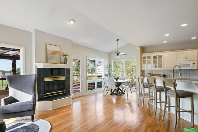 living room with ceiling fan, light hardwood / wood-style floors, a tiled fireplace, and vaulted ceiling