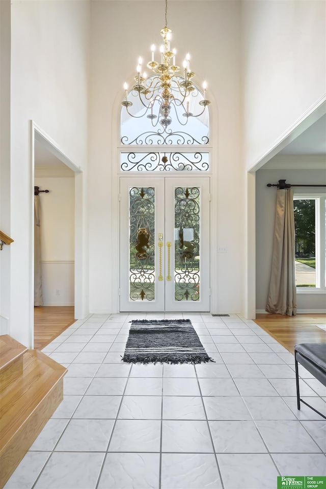 entryway with french doors, a towering ceiling, tile patterned floors, and a notable chandelier