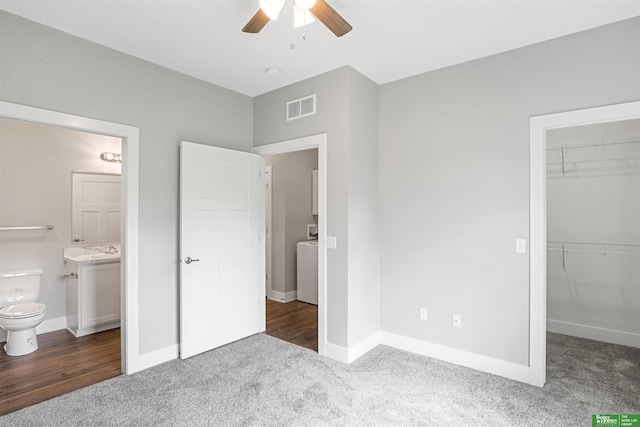 unfurnished bedroom featuring a walk in closet, ensuite bathroom, ceiling fan, dark colored carpet, and a closet