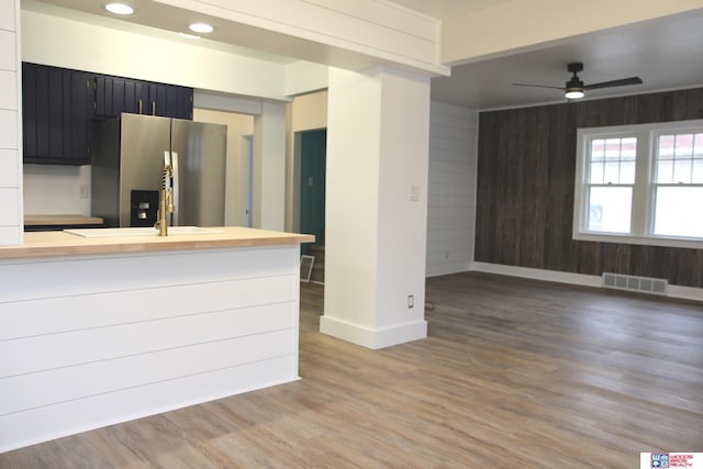 kitchen featuring wooden walls, ceiling fan, kitchen peninsula, wood-type flooring, and stainless steel fridge with ice dispenser