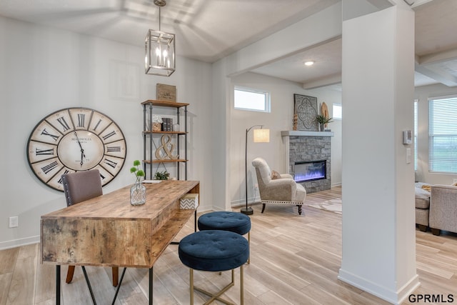 office with beam ceiling, a stone fireplace, light hardwood / wood-style flooring, and a healthy amount of sunlight