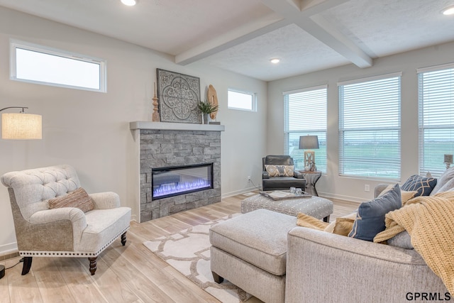 living room with beamed ceiling, a healthy amount of sunlight, a stone fireplace, and light wood-type flooring