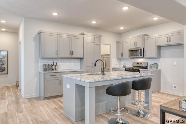 kitchen featuring stainless steel appliances, an island with sink, gray cabinetry, and light hardwood / wood-style floors