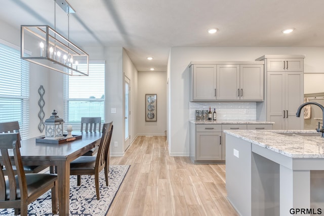 kitchen featuring sink, gray cabinetry, pendant lighting, light stone countertops, and light hardwood / wood-style floors