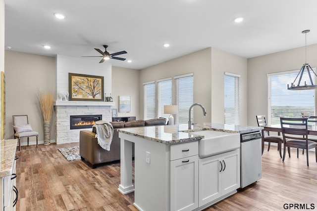 kitchen with stainless steel dishwasher, sink, pendant lighting, white cabinets, and an island with sink