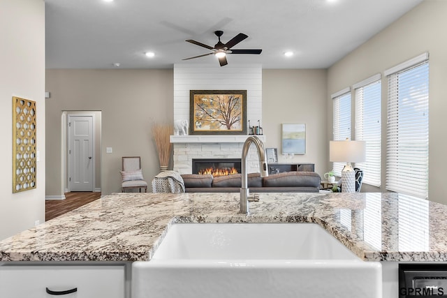 kitchen with ceiling fan, a large fireplace, light stone countertops, and sink