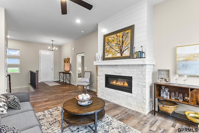 living room with a stone fireplace, hardwood / wood-style floors, and ceiling fan with notable chandelier