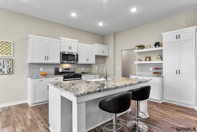 kitchen with appliances with stainless steel finishes, light stone counters, sink, white cabinets, and an island with sink