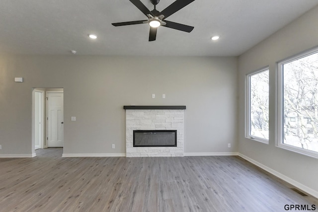 unfurnished living room with ceiling fan, light hardwood / wood-style floors, a stone fireplace, and a wealth of natural light