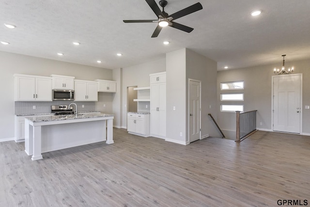 kitchen with a kitchen island with sink, white cabinets, ceiling fan with notable chandelier, hanging light fixtures, and stainless steel appliances