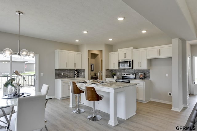 kitchen featuring a kitchen island with sink, decorative light fixtures, light hardwood / wood-style floors, white cabinetry, and stainless steel appliances