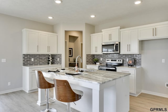 kitchen with a breakfast bar, stainless steel appliances, white cabinets, and a kitchen island with sink
