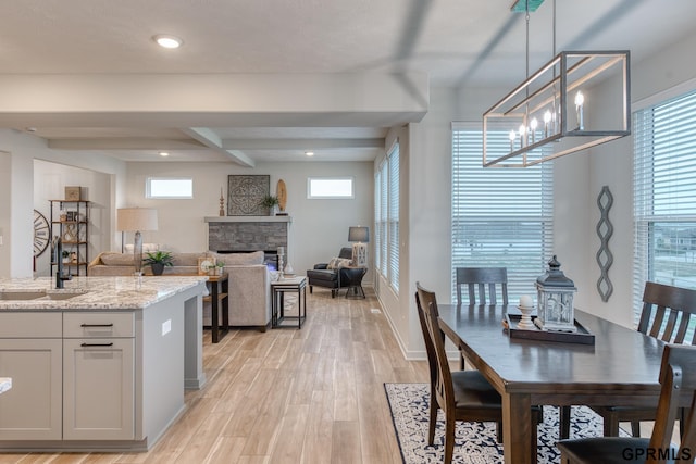 dining area with sink, a chandelier, beamed ceiling, a fireplace, and light hardwood / wood-style floors