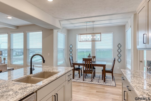 kitchen with light stone counters, sink, and decorative light fixtures