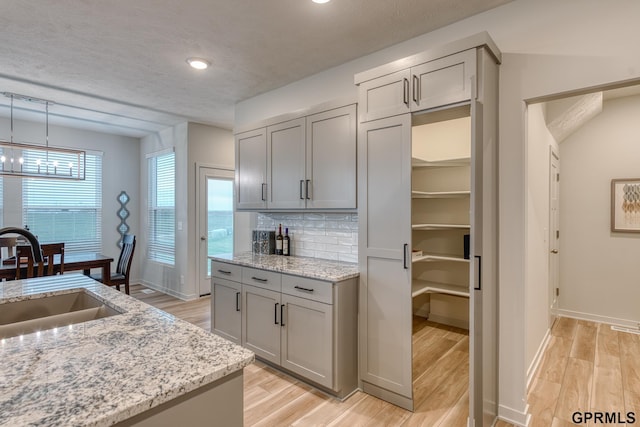 kitchen with light stone countertops, backsplash, gray cabinets, and sink