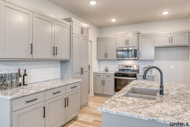 kitchen with light stone countertops, sink, light hardwood / wood-style flooring, gray cabinets, and appliances with stainless steel finishes