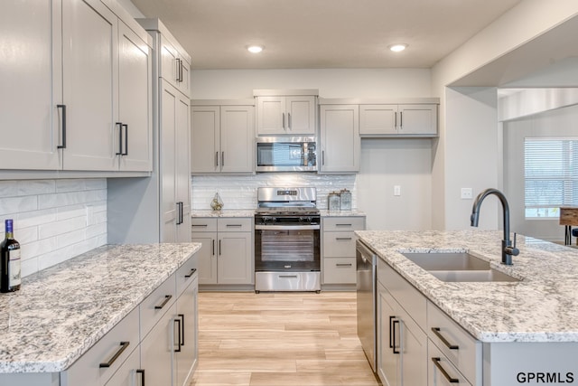 kitchen featuring a kitchen island with sink, sink, light stone counters, and appliances with stainless steel finishes