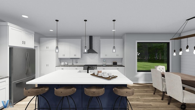 kitchen featuring wall chimney range hood, refrigerator, decorative light fixtures, a kitchen island with sink, and white cabinets