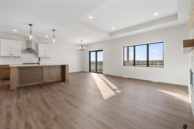 kitchen featuring wall chimney exhaust hood, a fireplace, a large island, white cabinetry, and wood-type flooring