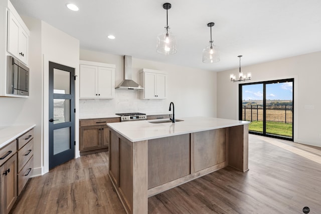 kitchen featuring appliances with stainless steel finishes, wall chimney exhaust hood, sink, a center island with sink, and white cabinetry