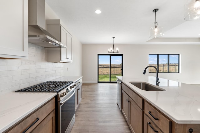 kitchen with pendant lighting, white cabinets, wall chimney range hood, sink, and appliances with stainless steel finishes