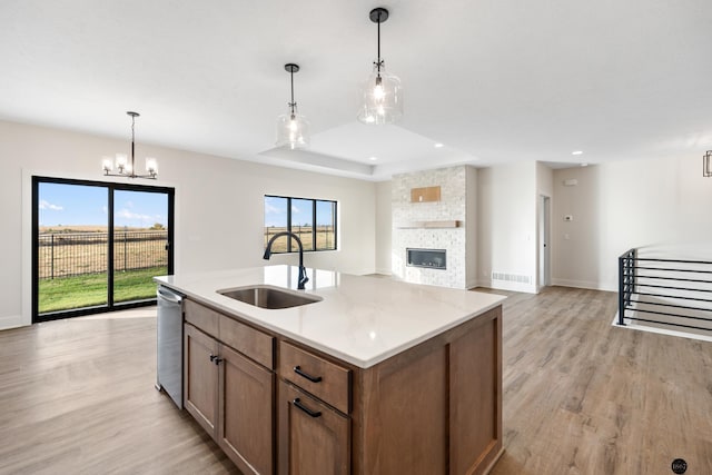 kitchen featuring dishwasher, sink, hanging light fixtures, a stone fireplace, and a center island with sink