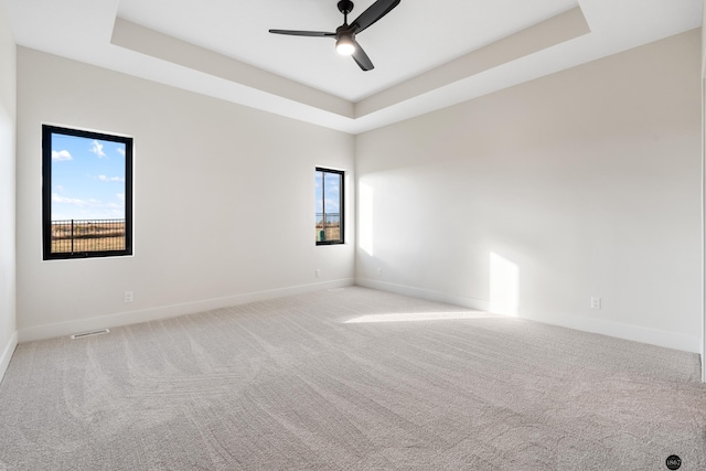 unfurnished room with a tray ceiling, ceiling fan, and light carpet