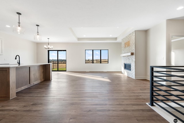 unfurnished living room featuring sink, a fireplace, a tray ceiling, a notable chandelier, and dark hardwood / wood-style flooring