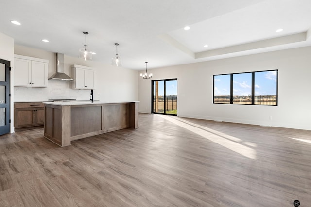 kitchen featuring white cabinetry, wall chimney range hood, light hardwood / wood-style flooring, a large island with sink, and plenty of natural light