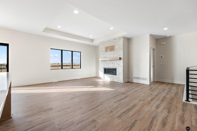 unfurnished living room featuring a tray ceiling, a stone fireplace, and light hardwood / wood-style floors