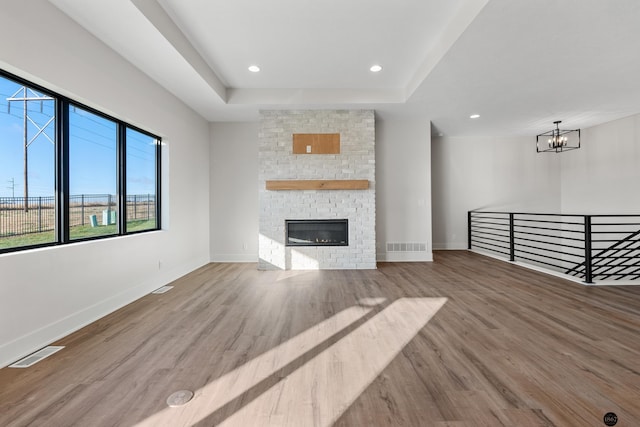 unfurnished living room with a tray ceiling, a fireplace, a notable chandelier, and hardwood / wood-style flooring