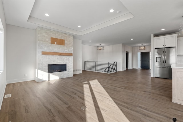 unfurnished living room featuring a raised ceiling, dark hardwood / wood-style flooring, and a brick fireplace