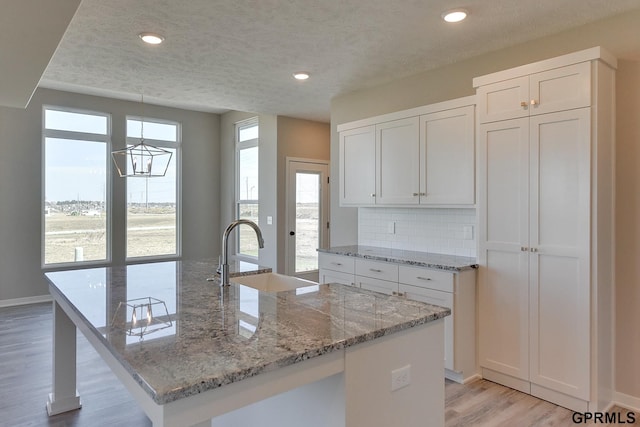 kitchen featuring decorative backsplash, a kitchen island with sink, sink, light hardwood / wood-style flooring, and white cabinets